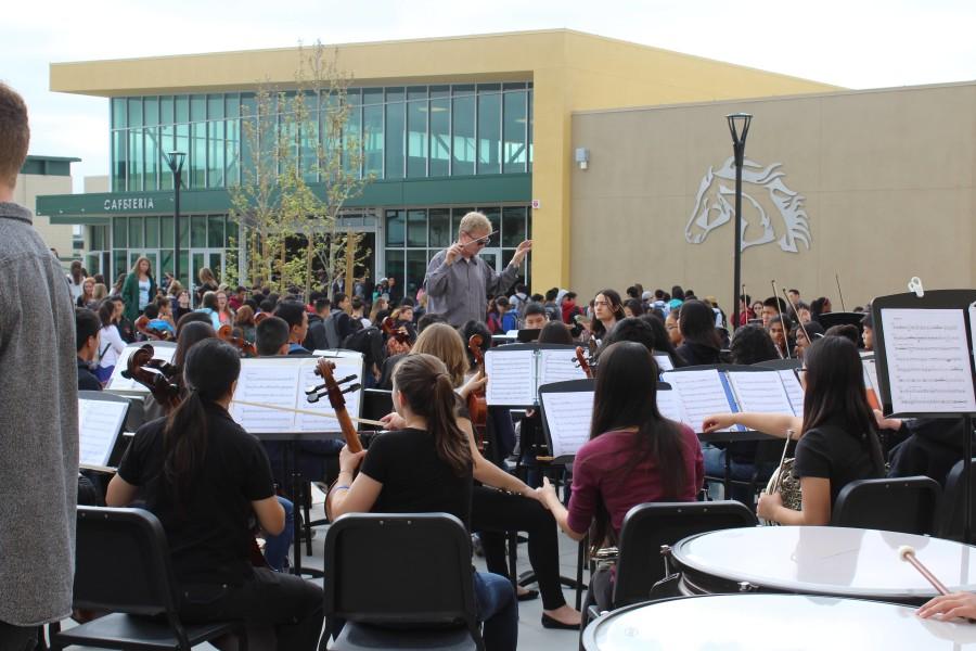 Music teacher John Burn conducts student orchestra and band performance.
