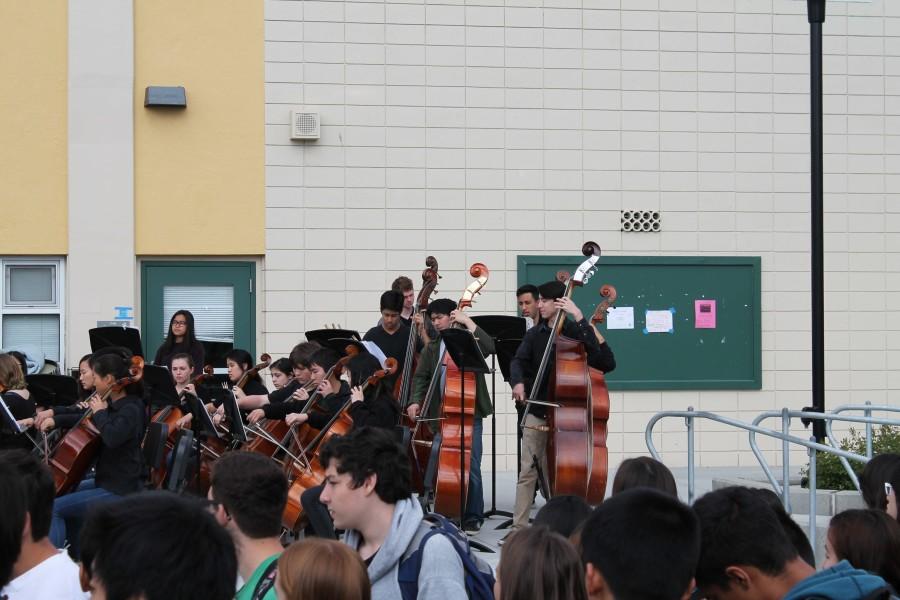 Symphony orchestras cello players performing a piece, while other students wait in line to purchase Club n Grub tickets.
