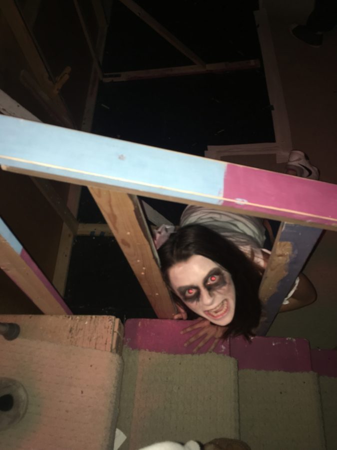 Drama Club member hides under stage staircase to scare groups walking through the house.