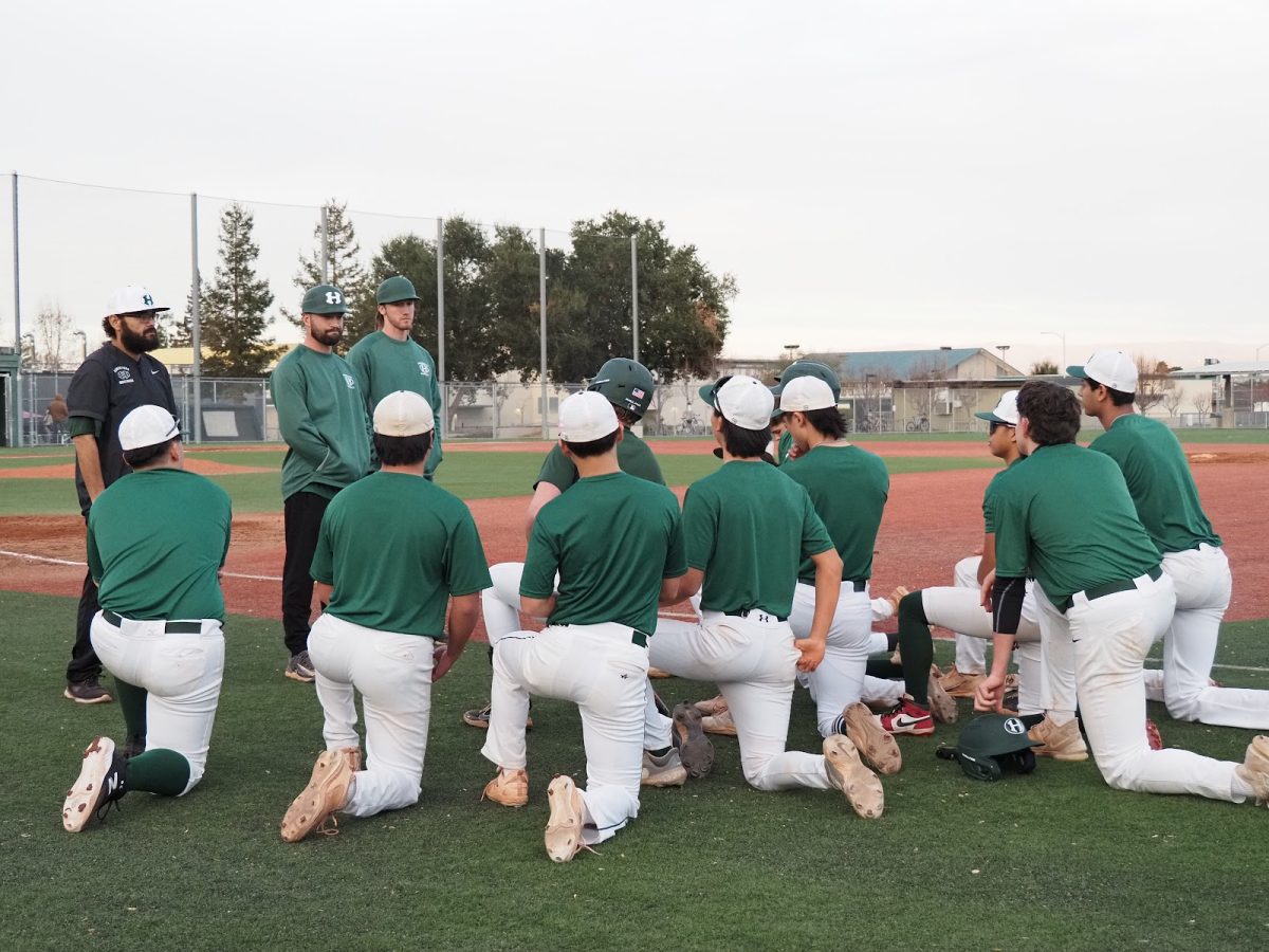 Baseball coaches Joseph Perez, Travis Sunseri and Dylan Remahl (from left to right) address the varsity team after their first scrimmage of the season on Feb. 13. The new coaches have worked with the players individually on how they can be more efficient with our movements, pitcher and first baseman Nate Enders said.