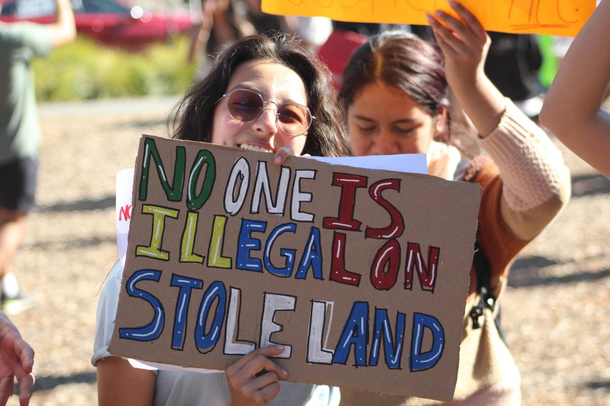 One attending student smiles as she holds up a multicolored message with white highlights. 